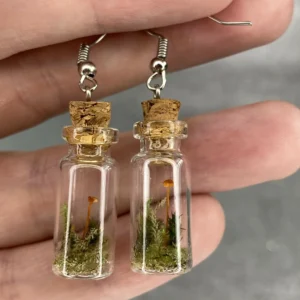 A pair of glass bottle earrings with a cork on top with mushrooms and moss arranged inside.